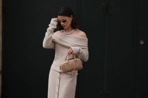 Lea Naumann is seen wearing oval sunglasses with a golden frame, small silver hoop earrings with heart pendants, a pearl necklace, and a silver...