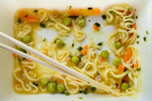 leftovers of eaten instant noodles sprinkled with spices, vegetables, herbs and freeze-dried meat. there are wooden chopsticks nearby. asian chicken soup with ramen noodles on the dining kitchen table. the end of the meal. si