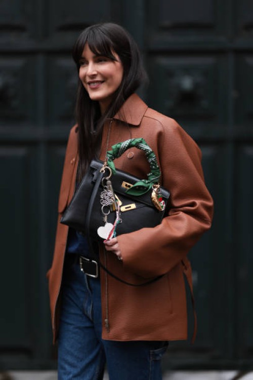 Leia Sfez is seen wearing a brown leather Hermes jacket, blue denim jeans, black belt and Hermes black bag with Kelly twilly charms outside Hermes...