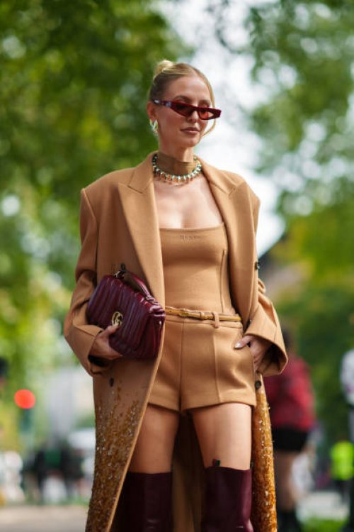 Leonie Hanne wearing a camel-colored coat over a matching top with sequined embellishments, and burgundy knee-high boots, a necklace, red sunglasses,...