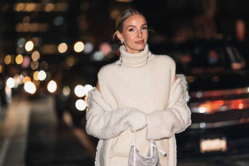 Leonie Hanne wears a black and large rhinestones pendant earrings, a white wool turtleneck sleeveless oversized pullover, a white fluffy long coat, a...