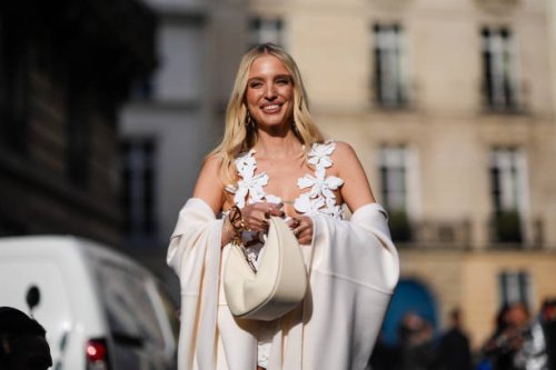 Leonie Hanne wears a Valentino bangle, a white guipure lace micro dress, a cream color bag, a cream color wool cape , outside Valentino , during the...