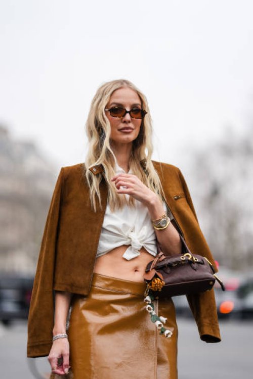 Leonie Hanne wears dark brown sunglasses, white collar tied Miu Miu shirt, dark brown unzipped Miu Miu suede jacket, gold Cartier Bracciale Juste...