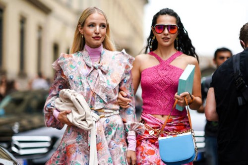Leonie Hanne wears earrings, a pink turtleneck, a long sleeves, ruffled, light pink dress with colorful flowers print and a lavaliere, a white belt...