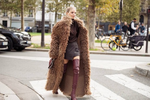 Leonie Hanne wears long over knee burgundy leather boots, burgundy mini skirt, burgundy top, brown fur coat and burgundy bag and sunglasses outside...