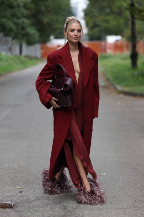 Leonie Hanne wears red long dress, red coat, burgundy and white fringed heels, burgundy Ferragamo big bag, outside Ferragamo, during the Milan...