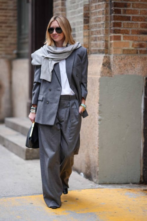 Lisa Aiken wears a light gray scarf, a dark gray oversized blazer jacket, a white t-shirt, matching suit pants, a black leather bag, outside Proenza...