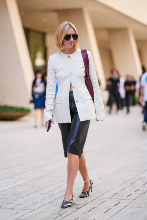 Lisa Aiken wears black sunglasses, white blazer jacket, shiny dark brown leather bag, shiny black over the knee skirt, black and white striped heels,...
