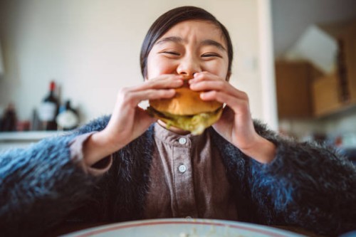 lovely cheerful girl enjoying her homemade burger at home - junk food stock pictures, royalty-free photos & images