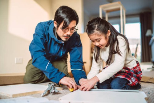 lovely cheerful girl helping her dad to assemble furniture in their new home - home decoration stockfoto's en -beelden