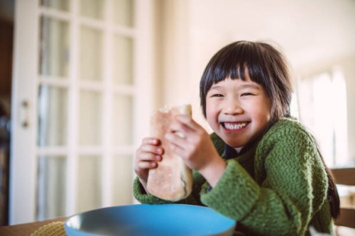 lovely cheerful girl smiling joyfully at the camera while enjoying snack with her sister in front of a food stall in the street - junk food stock pictures, royalty-free photos & images