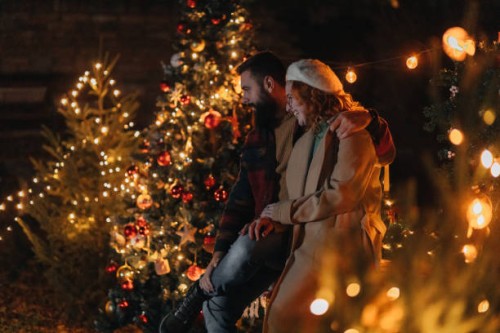 lovely couple next to a beautifully decorated christmas tree - garden decoration stock pictures, royalty-free photos & images