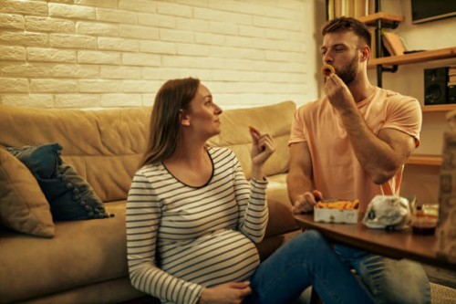 lovely man and his pregnant woman eating onion rings at home - junk food stock pictures, royalty-free photos & images