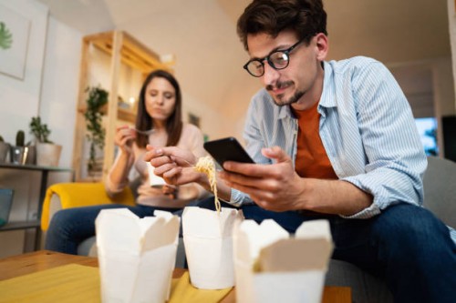 low-angle view of a young man using a phone while eating - junk food stock pictures, royalty-free photos & images