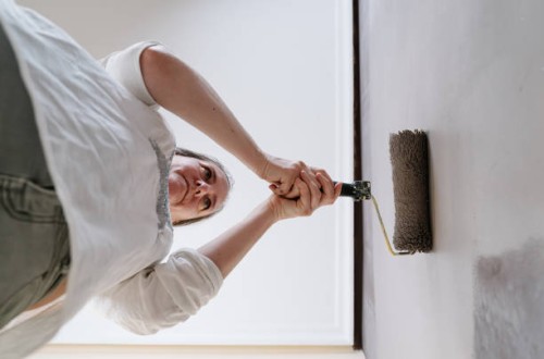 low angle of woman catching with two hands a roller of grey painting on a brown wall. - home decoration stock pictures, royalty-free photos & images