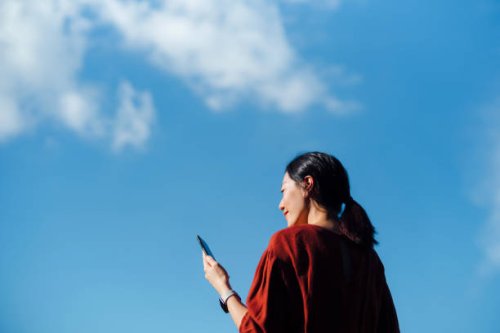 low angle portrait of young asian woman using smartphone against beautiful blue sky with cloudscapes, enjoying sunlight outdoors. lifestyle and technology - travel stock pictures, royalty-free photos & images