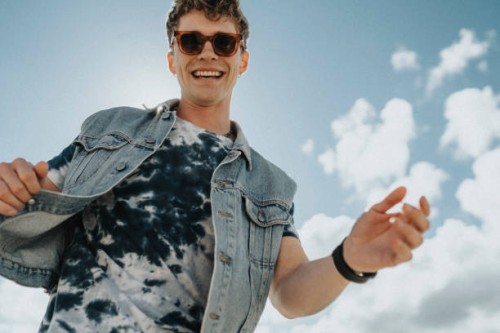low angle view of happy young man with tattooed arm dancing under cloudy sky - fashion stock pictures, royalty-free photos & images