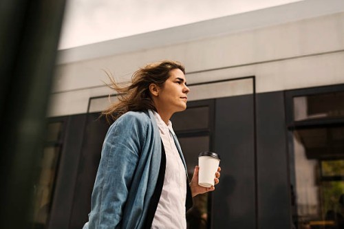 low angle view of young woman holding disposable cup while walking by tram - junk food stock pictures, royalty-free photos & images