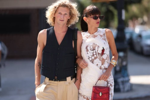 Luca Fröhlingsdorf seen wearing navy blue textured buttoned suit vest, black leather belt, beige long pants; Katya Tolstova wears burgundy red...