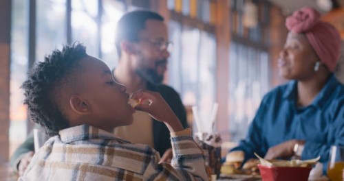 lunch, eating and boy with parents in restaurant with food, conversation or hungry kid at table. black family, mother and father with child in cafe for burger, drinks and bonding on weekend in africa - junk food stock picture