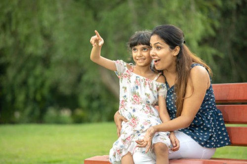mère enjouée avec sa fille assise sur un banc contre des arbres luxuriants dans un parc - garden decoration photos et images de collection