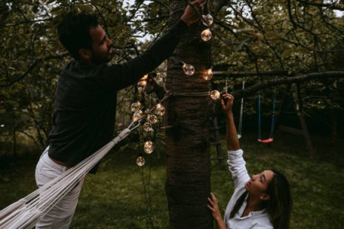 male and female friends hanging lighting equipment in backyard during dinner party - garden decoration stock pictures, royalty-free photos & images