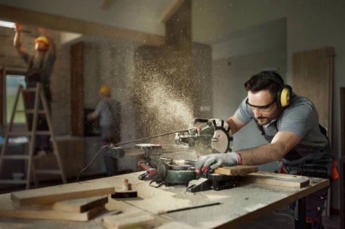 male carpenter cutting wood plank with electric saw at construction site. - home decoration stock pictures, royalty-free photos & images