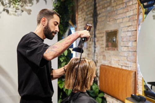 male hairdresser drying the hair of a client sitting in front of a mirror in a modern hairdressing salon. - hairstyle stock pictures, royalty-free photos & images