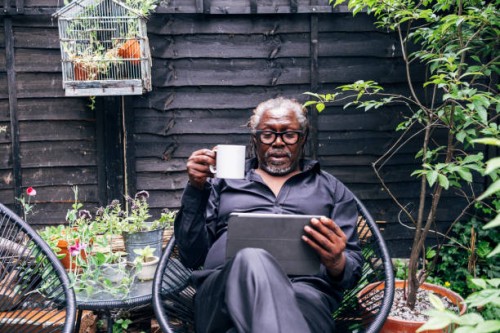 male professional holding mug looking at digital tablet while sitting on chair in backyard - garden decoration photos et images de collection