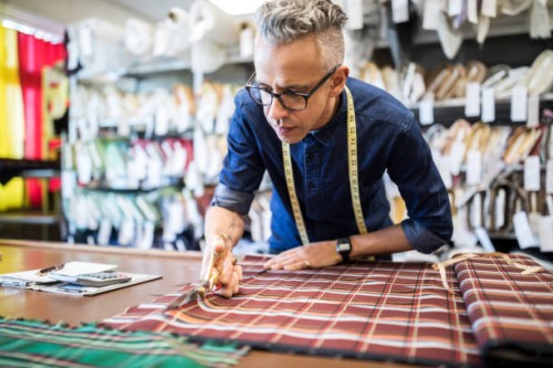 male tailor cutting a textile at workbench - fashion stock pictures, royalty-free photos & images