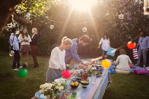 man and woman preparing food at dining table with friends in background during summer party - garden decoration stock pictures, royalty-free photos & images