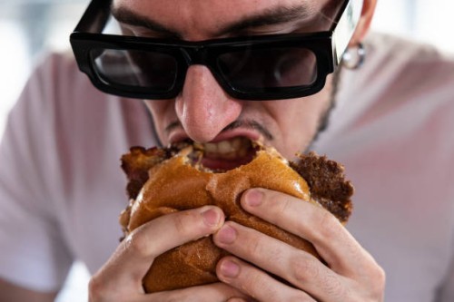 Man bites a bacon cheeseburger at Meat Crew fast food restaurant on May 28, 2023 in Milan, Italy. On occasion of the World Burger Day, celebrated on...
