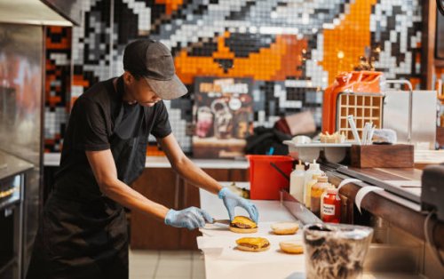 man, burger and fast food kitchen worker at counter with gloves, cooking and uniform at small business. restaurant, sandwich and cook with hamburger patty stack for lunch service with take away. - junk food stock pictures, ro