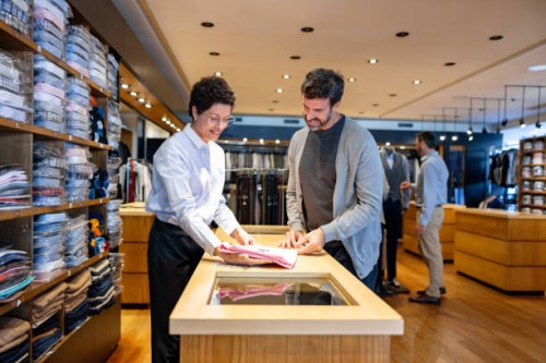 man buying clothes at a clothing store with the help of a retail clerk - fashion stock pictures, royalty-free photos & images