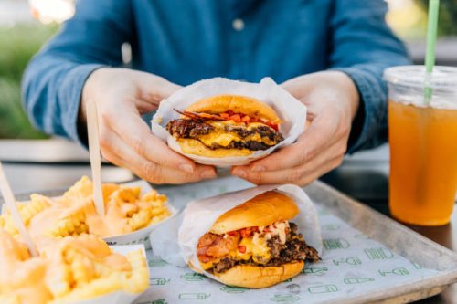 man eating cheeseburger and cheese fries at fast food joint - junk food stock pictures, royalty-free photos & images