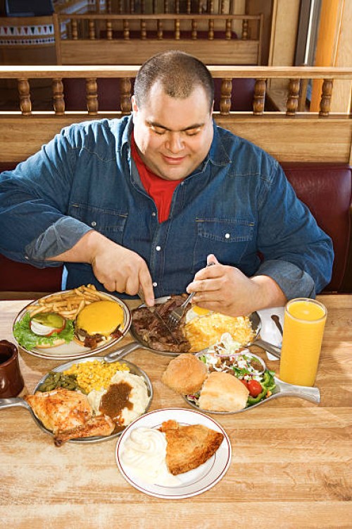 man eating from multiple plates of food in restaurant - junk food stock pictures, royalty-free photos & images