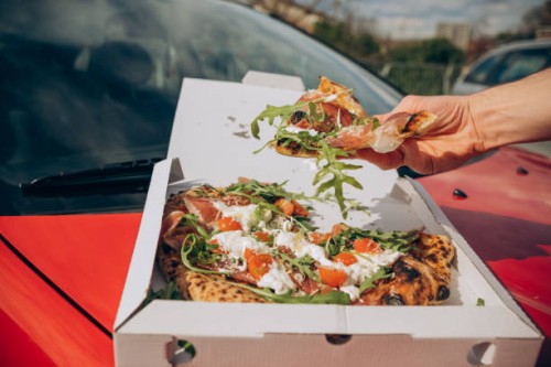 man eating pizza on the hood of a red car in a parking lot male hands - junk food stock pictures, royalty-free photos & images
