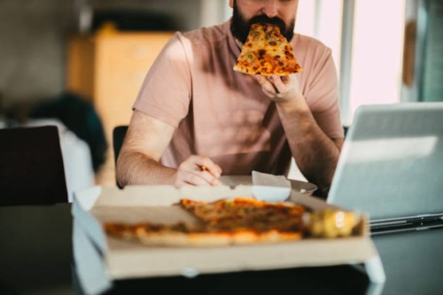 man eating take-out pizza, using laptop and working from home - junk food stock pictures, royalty-free photos & images