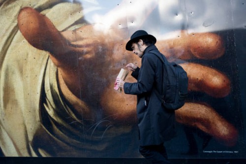 Man eats while walking past a large detail reproduction of Caravaggio's 'The Supper of Emmaus' outside the National Gallery that is in 2023,...