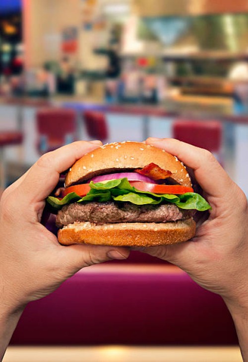 man holding a hamburger in a diner - junk food stock pictures, royalty-free photos & images