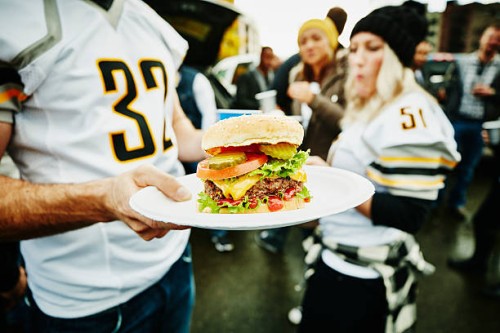 man holding burger on plate at tailgating party - food stock pictures, royalty-free photos & images