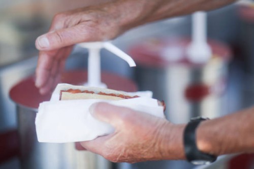 man putting tomato sauce on a hotdog - junk food stock-fotos und bilder
