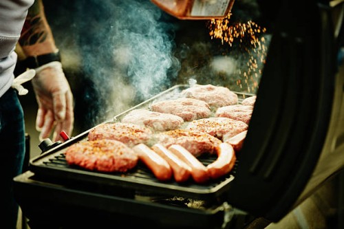 man seasoning burgers and hot dogs on barbecue - food fotografías e imágenes de stock