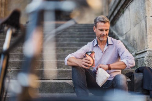 man sitting on stairs with takeaway coffee in the city checking the time - junk food stock pictures, royalty-free photos & images