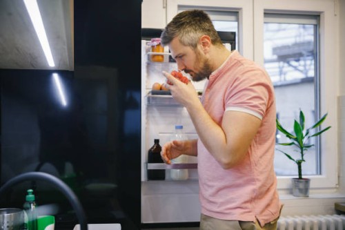man standing in the kitchen, holding a box of cherry tomatoes and smelling it - food stock pictures, royalty-free photos & images