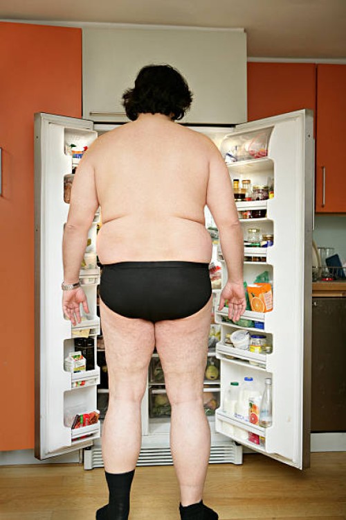 man wearing underwear, standing by open fridge, rear view - junk food stock-fotos und bilder