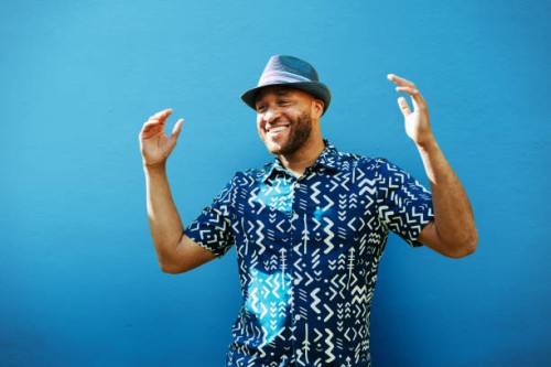 man with arms up, smiling, next to blue wall - fashion stock pictures, royalty-free photos & images
