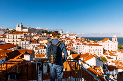 man with backpack looking at lisbon old town cityscape from a scenic viewpoint (miradouro), portugal - travel stock-fotos und bilder