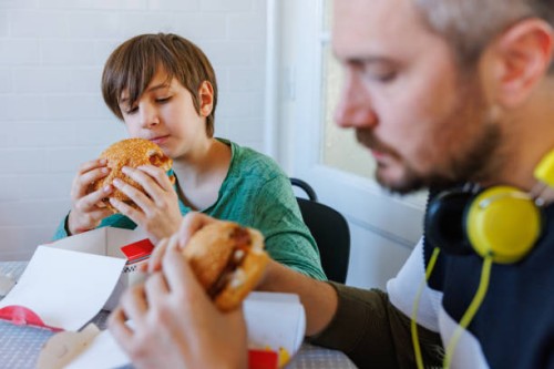 man with headphones and his preadolescent son having take out burgers at the table - junk food stock pictures, royalty-free photos & images