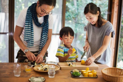 man, woman and boy standing at a table, preparing corn on the cob, smiling. - food stock pictures, royalty-free photos & images